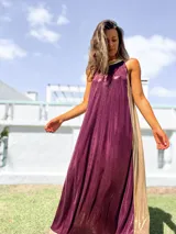 Vestido largo de fiesta con diseño bicolor, presentando un panel frontal en color bordó y paneles laterales en color dorado. Confeccionado en tela brillante con caída fluida, presenta escote halter y corte holgado.