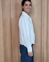 Camisa de color arena con mangas abullonadas, puños anchos con botones y cuello clásico. Presenta un diseño de corte recto con costuras visibles y cierre frontal oculto.