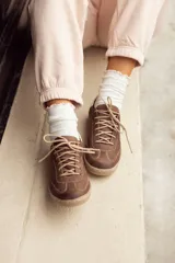 Zapatillas acordonadas de cuero color marrón chocolate, con detalle en blanco en el talón y suela color caramelo.