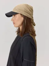 Gorro tipo pañuelo con visera rígida azul marino, confeccionado en lino con estampado de rayas grises y blancas. Presenta un diseño envolvente con caída trasera y detalle de logo bordado en el lateral.
