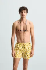 Bañador de hombre de tejido técnico ripstop, color mostaza con estampado floral abstracto en blanco y negro. Presenta cintura elástica ajustable con cordón, bolsillos laterales y bolsillo trasero de plastrón.