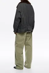 Cazadora corta de corte cruzado confeccionada en mezcla de algodón lavado color gris oscuro. Presenta un cuello camisero con pelo sintético desmontable en color marrón, cierre frontal con botones de presión y mangas largas con trabillas en los puños. Incluye bolsillos laterales, espalda fruncida en la cintura y trabillas ajustables laterales para definir la silueta.