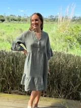 Vestido midi de lino color verde oliva, con cuello mao, escote con botones de nácar, mangas tres cuartos con volados y ruedo con volado.