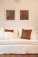 Almohadón decorativo cuadrado, con frente de cuero color marrón y parte trasera de tussor color blanco hueso.