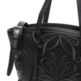 Cartera grande negra con diseño calado floral y logo metálico circular en el frente. Tiene doble asa corta, cierre superior y correa larga desmontable con hebilla.