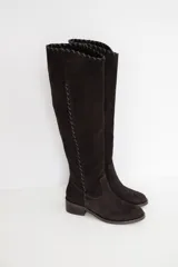 Bota alta de caña larga confeccionada en cuero color chocolate, con detalle de pespuntes decorativos a lo largo de la caña y en el borde superior, y taco bajo cuadrado.