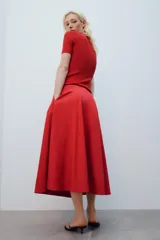 Falda midi de tiro alto y corte en A, color rojo, con bolsillos laterales ocultos y cierre lateral con cremallera.