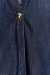 Camisa de denim azul oscuro con corte amplio, cuello solapa, escote en pico y mangas tres cuartos. Presenta un aplique metálico dorado en el centro y bajo asimétrico.