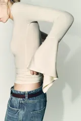 Camiseta de cuello redondo y manga larga, confeccionada en tejido rib con mezcla de lyocell. Presenta un diseño ajustado con terminación de volantes en los puños y bajo recto.