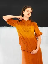 Blusa color ocre de algodón tipo seda, teñida a mano con técnica tie dye. Tiene corte recto, cierre invisible en el escote delantero y mangas regulables con elástico.