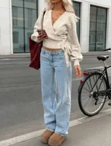 Sweater de punto tipo wrap, color beige, con escote en V profundo, mangas largas con puños ajustados y cierre cruzado mediante lazo lateral.