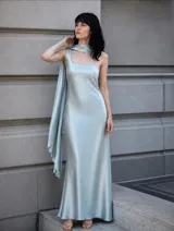 Vestido largo de seda en color celeste, con diseño de un solo hombro y una capa integrada que cae desde el cuello hacia atrás.
