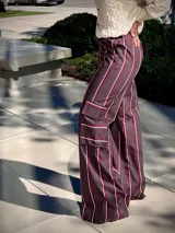 Pantalon de corte cargo con diseño a rayas verticales en tonos marrón, blanco y bordó. Presenta bolsillos laterales tipo cargo, tiro alto y pernera ancha.
