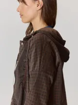 Campera de corte holgado con textura aterciopelada y estampado de cuadros sutil. Presenta cuello con cordones ajustables, cierre frontal con botones y mangas largas con puños elásticos.