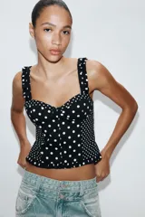 Top estilo corset con escote corazón, tirantes anchos con detalle de fruncido y cierre posterior con cremallera. Presenta un diseño de estampado de lunares en contraste.