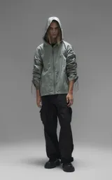 Campera rompevientos de diseño oversize, color verde, confeccionada en microfibra técnica ligera. Presenta capucha integrada, cierre frontal técnico y un sistema de frunces elásticos regulables a lo largo de las mangas que permiten ajustar el volumen de la prenda.