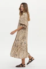 Vestido túnica de lino y viscosa, color camel con estampa artesanal en tonos oscuros, escote en V profundo, mangas amplias abullonadas y falda larga con volado en el ruedo.