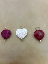 Dije con forma de corazón de piedra sintética en varios colores con gancho metálico dorado.