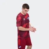Remera deportiva Umbro modelo Press, de color rojo con un estampado abstracto en tonos más oscuros, cuello redondo y manga corta. Incluye el logo de la marca en el pecho y el escudo del Club Nacional de Football.