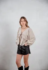 Camisa de lino color beige con escote en V, mangas largas abullonadas y detalle de frunces con cordón ajustable en la parte frontal.