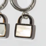 Par de aros argolla plateados con dije colgante en forma de candado con frente de nácar.