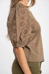 Remera de algodón color rosado con mangas cortas abullonadas de broderie con diseño floral calado. Presenta cuello redondo y costura vertical central en el frente.