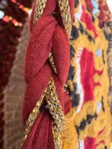 Bolso tejido a mano con hilo de trapillo, eco-cuero y textiles, con un diseño central de querubín coronado y alas, sobre un fondo de franjas rojas, blancas y azules. Posee asas cortas tejidas en color celeste claro.