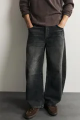 Jeans de denim de algodón color gris con efecto lavado, de corte relaxed barrel fit y tiro medio. Presenta diseño amplio con pinzas en las rodillas y costuras curvas, cierre frontal con botones y cinco bolsillos tradicionales.