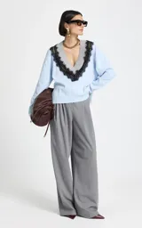 Sweater de punto color celeste con escote en V profundo, ribete acanalado gris y aplicación de encaje negro que delinea el escote. Presenta mangas largas con puños acanalados y dobladillo acanalado.