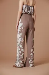 Pantalón de tiro alto con silueta amplia y corte recto, confeccionado en tela fluida color marrón con estampado botánico en tonos claros en los laterales.