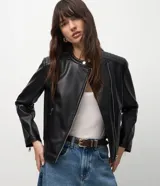 Campera biker de poliuretano color negro, de corte entallado, con cierre frontal cruzado, bolsillos laterales con cremallera, cuello mao con botón a presión y detalles capitonados en los hombros.