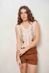 Chaleco de crochet color beige, sin mangas, con escote en V y botones frontales. Cuenta con bordados florales en tono marrón, celeste y ocre en la parte delantera y diseño con ondas en el ruedo.