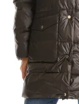 Campera puffer larga de color marrón oscuro, con diseño capitoneado de costuras horizontales. Presenta un sistema de cierre doble con pechera interna fija con cierre y cuello alto, y cierre frontal exterior con botones a presión. Incluye bolsillos frontales amplios, capucha fija y cierres laterales en el ruedo para mayor movilidad.