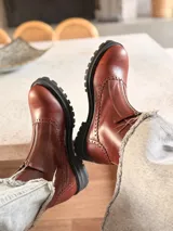 Botas de cuero color marrón rojizo con diseño estilo brogue, cierre lateral y suela track negra de goma resistente.