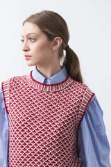 Chaleco tejido de algodón y acrílico, color rojo y blanco con patrón geométrico. Tiene cuello redondo y bordes acanalados en rojo.