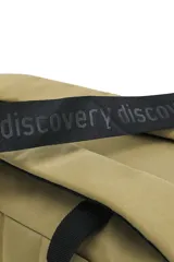 Mochila cilíndrica color beige/camel, con tres compartimentos apilados cerrados con cremallera negra. Presenta el logo "Discovery" bordado en la parte superior y el mismo texto repetido tres veces en la parte inferior. Incluye asa superior y correa ajustable para llevar al hombro.