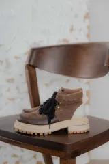 Botas acordonadas de caña baja con diseño combinado en gamuza marrón, cuero marrón oscuro en la puntera y detalle en cuero beige en el talón. Presenta suela track robusta en tono crema y cordones negros.