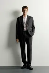 Pantalón de traje slim fit para hombre, color gris oscuro, con bolsillos frontales y bolsillos traseros de doble vivo con botón. Cuenta con cierre frontal de cremallera y botón, y presillas para cinturón.