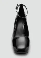 Zapato de tacón alto y ancho, color negro con acabado charol, punta cuadrada y tira ajustable con hebilla al tobillo.