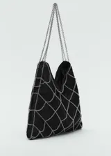 Bolso de mano pequeño con diseño de red de cadenas metálicas plateadas sobre una base de tejido de guipur negro. Cuenta con asas cortas de cadena.