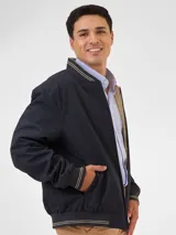 Campera bomber reversible azul marino y beige con cuello, puños y ruedo acanalados con rayas doradas. Tiene cierre frontal y logo bordado en el pecho.