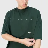 Remera de corte oversize color verde oscuro, con estampa gráfica en la espalda que incluye texto y diseño lineal.