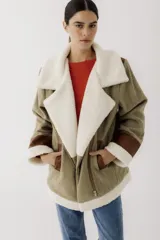 Gamulán de paño en color beige jaspeado con detalles en cuero sintético marrón y forro de corderito sintético blanco. Presenta cierre frontal cruzado, cuello solapa, bolsillos laterales y puños con vuelta.