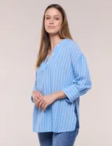 Blusa de silueta holgada a rayas verdes y blancas, confeccionada en tela liviana con textura arrugada. Presenta cuello en V profundo con botones frontales, mangas 3/4 de hombro caído y ruedo asimétrico con aberturas laterales.