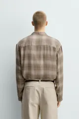 Camisa relaxed fit de manga larga con cuello solapa, confeccionada en tejido con mezcla de viscosa. Presenta un bolsillo plastrón en el pecho, bajo con aberturas laterales y cierre frontal de botonadura. El diseño es a cuadros en tonos beige y marrón.