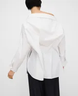 Camisa blanca de algodón con diseño desestructurado, escote asimétrico que deja un hombro al descubierto, manga larga y botonadura frontal.