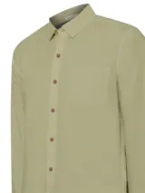 Camisa de manga larga color verde sage, confeccionada en popelina de algodón orgánico. Presenta cuello camisero, cierre frontal con botones de madera, bolsillo en el pecho con logo bordado y mangas ajustables con botones.