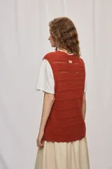 Chaleco de punto color beige, sin mangas, con escote redondo y cierre frontal con botones carey. Presenta diseño calado y silueta amplia.