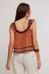 Musculosa blanca de poliéster con diseño romántico, tirantes con volados, detalles de encaje y cierre frontal con cordón ajustable y botones.