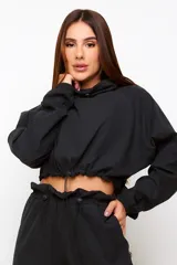 Buzo cropped negro de estilo urbano, con cuello alto ajustable mediante cordón, mangas largas con puños elásticos y cintura con ajuste regulable.